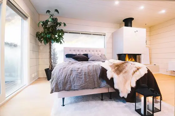 Muhkea vaaleankankainen jenkkisänky sisustettuna lappiaiheiseen moderniin huoneeseen takkatulen ääreen.